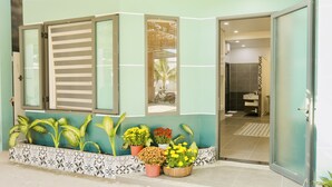A modern building with a teal facade, a large window with horizontal blinds, and a variety of potted plants in front. - Kiwi's Homestay & Cafe (Mui Ne)