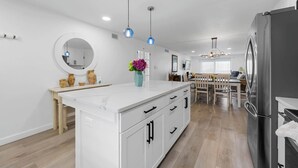 Une cuisine moderne avec des meubles blancs, un îlot central, un miroir rond et des luminaires suspendus.