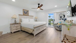 Une chambre à coucher comprenant un lit, des tables de chevet, un ventilateur de plafond, une fenêtre avec vue et un petit balcon.
