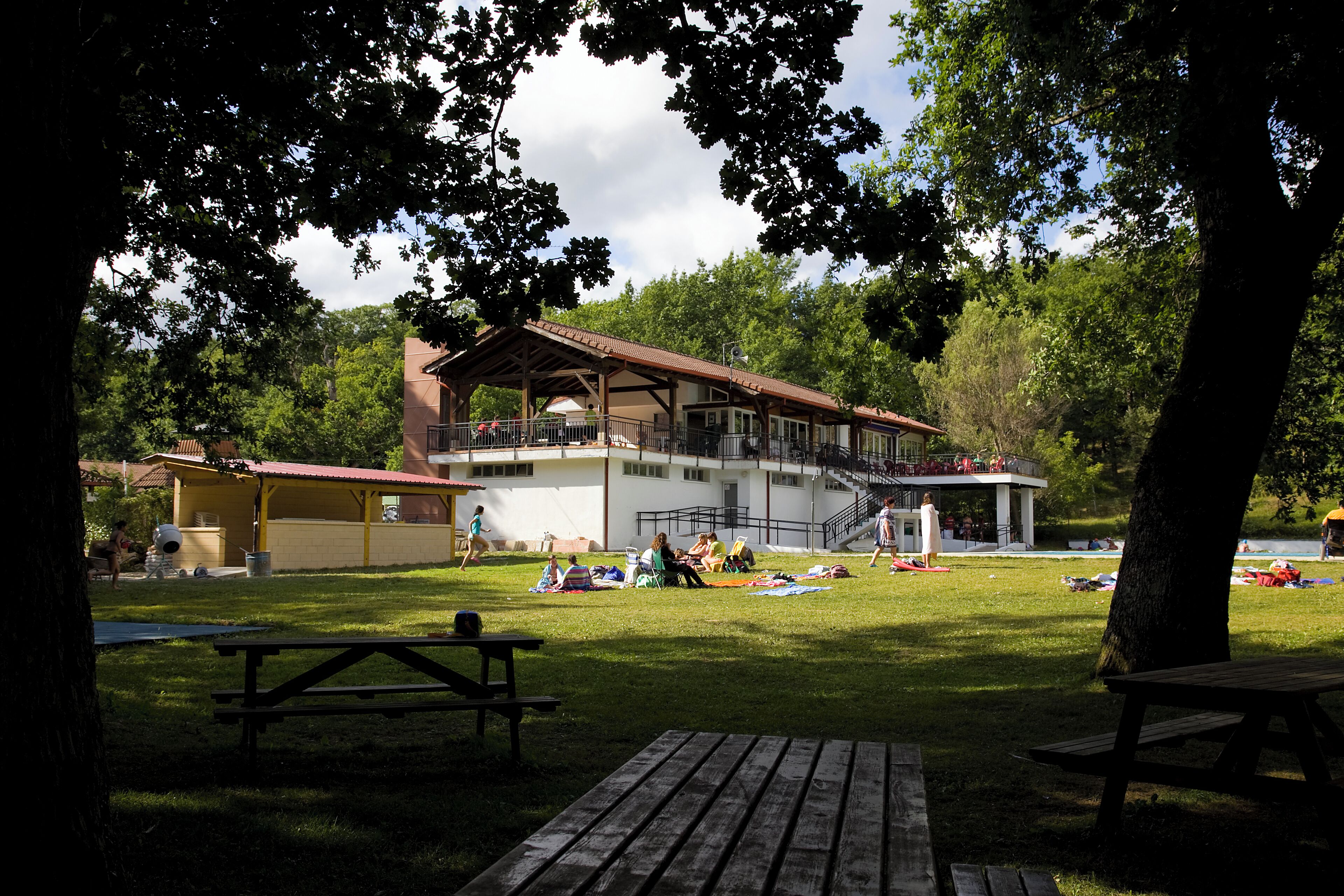Un parque con mesas de picnic, un pabellón cubierto y un edificio con balcón.