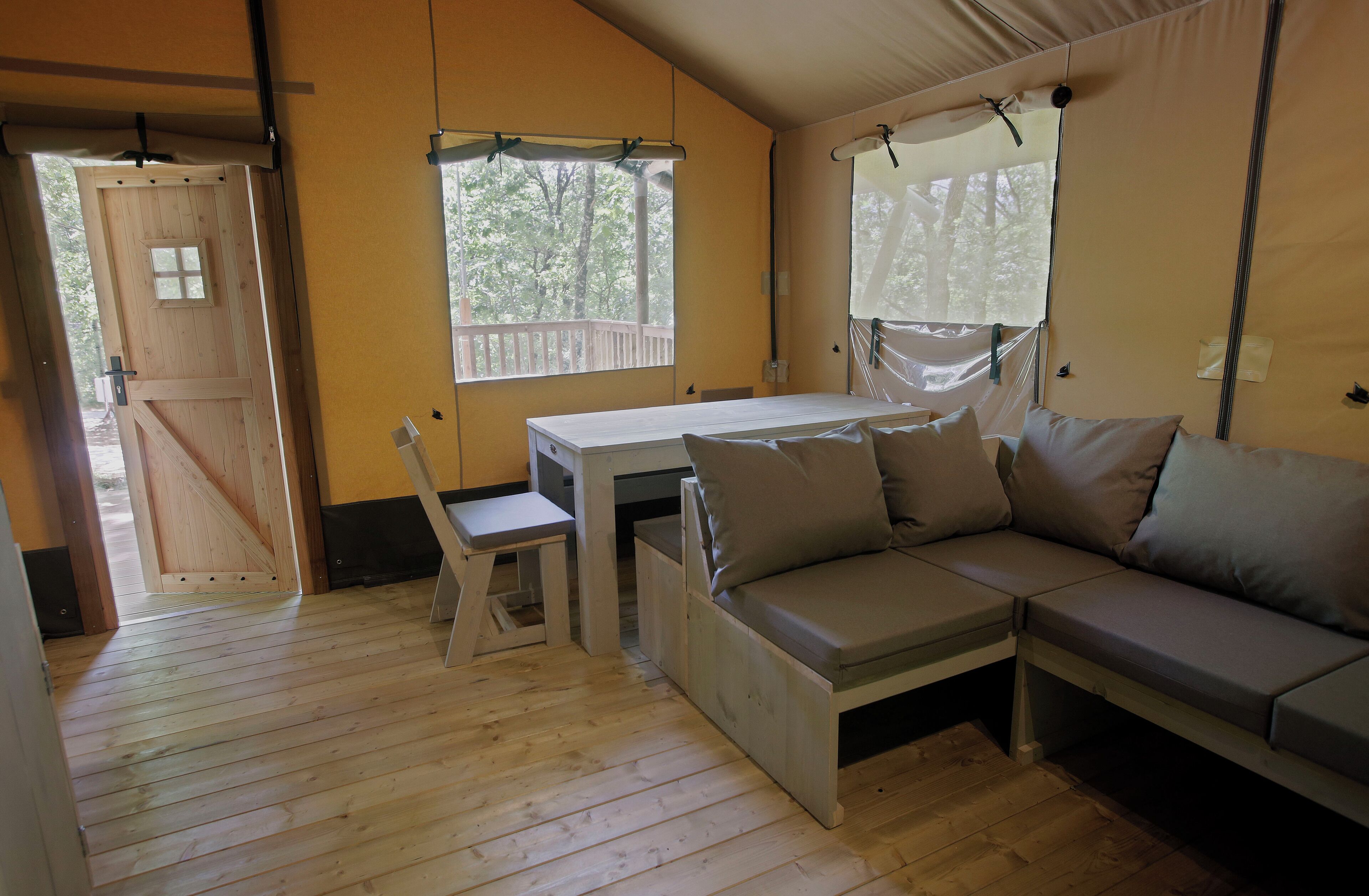 Una habitación acogedora con suelo de madera, una mesa blanca, un sofá y una ventana con vistas a árboles.