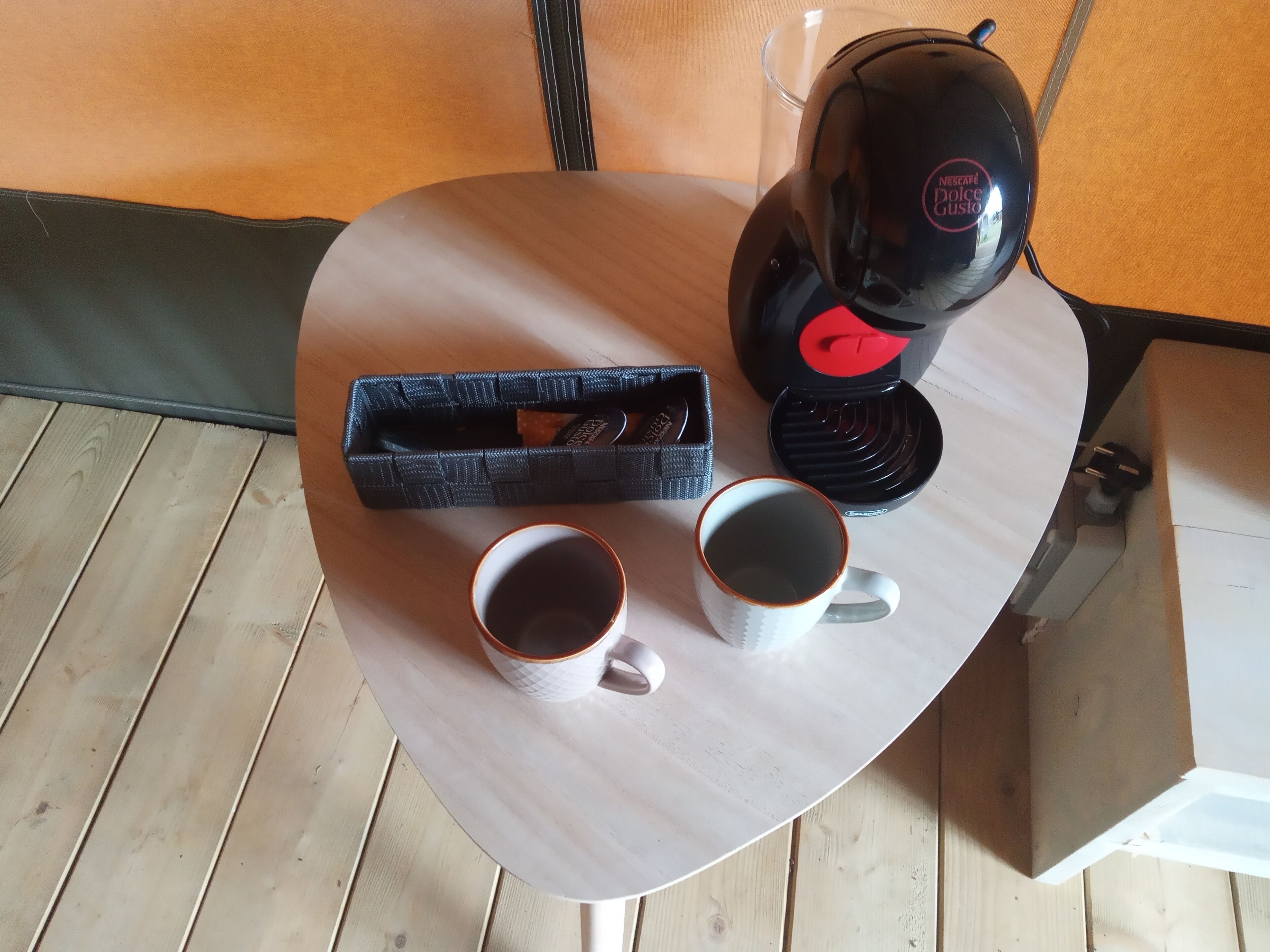 Una mesa redonda con una cafetera, dos tazas de café y una cesta de biscotti.
