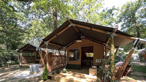 Una cabaña rústica con un porche cubierto, un espacio al aire libre para sentarse y una zona de descanso con cama y ventana.