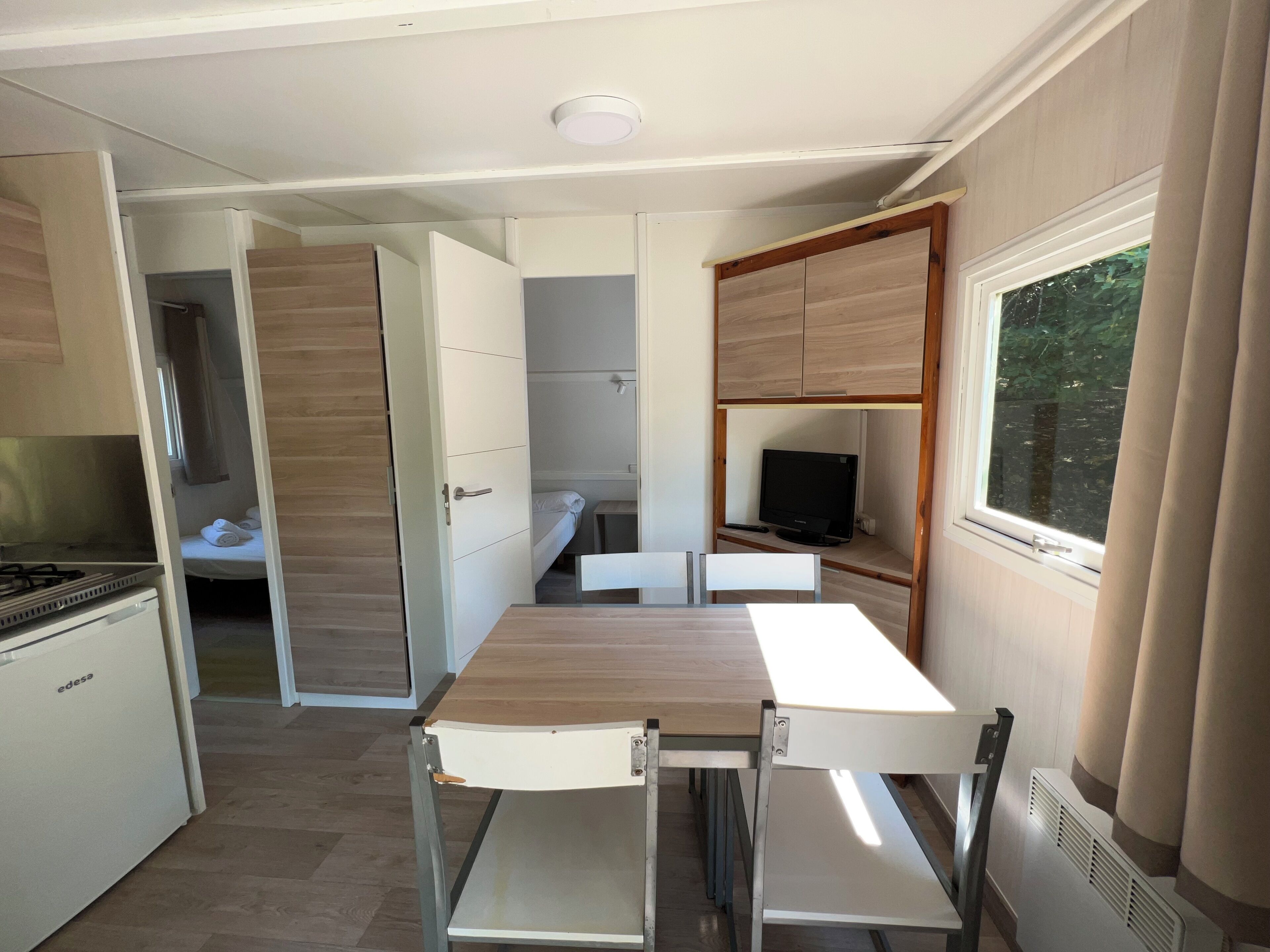 Een compacte kitchenette met een kookplaat, een kleine koelkast en een bed met een televisie in de hoek.