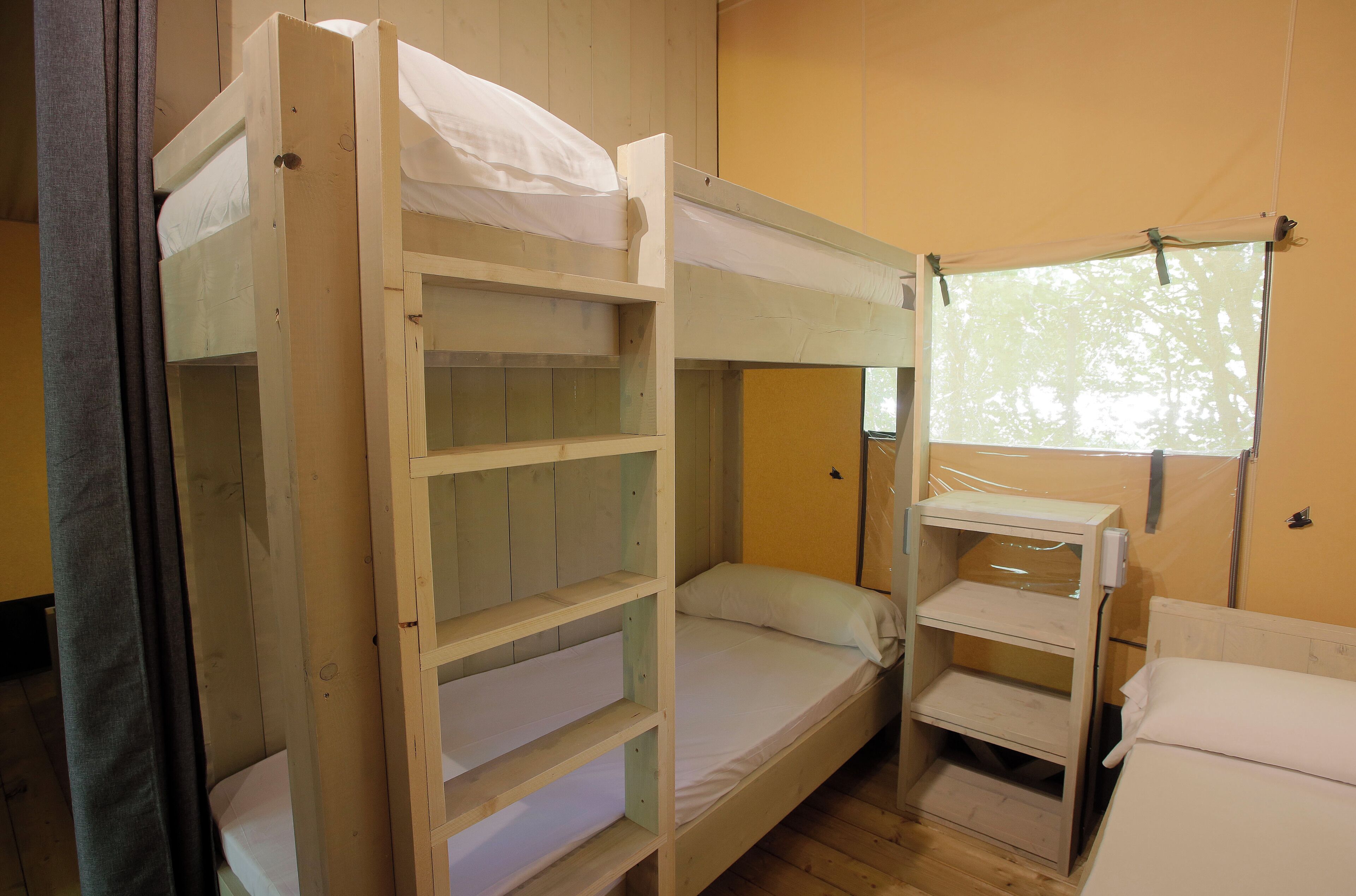 Ein Schlafraum mit Etagenbett, Fenster und Vorhang.