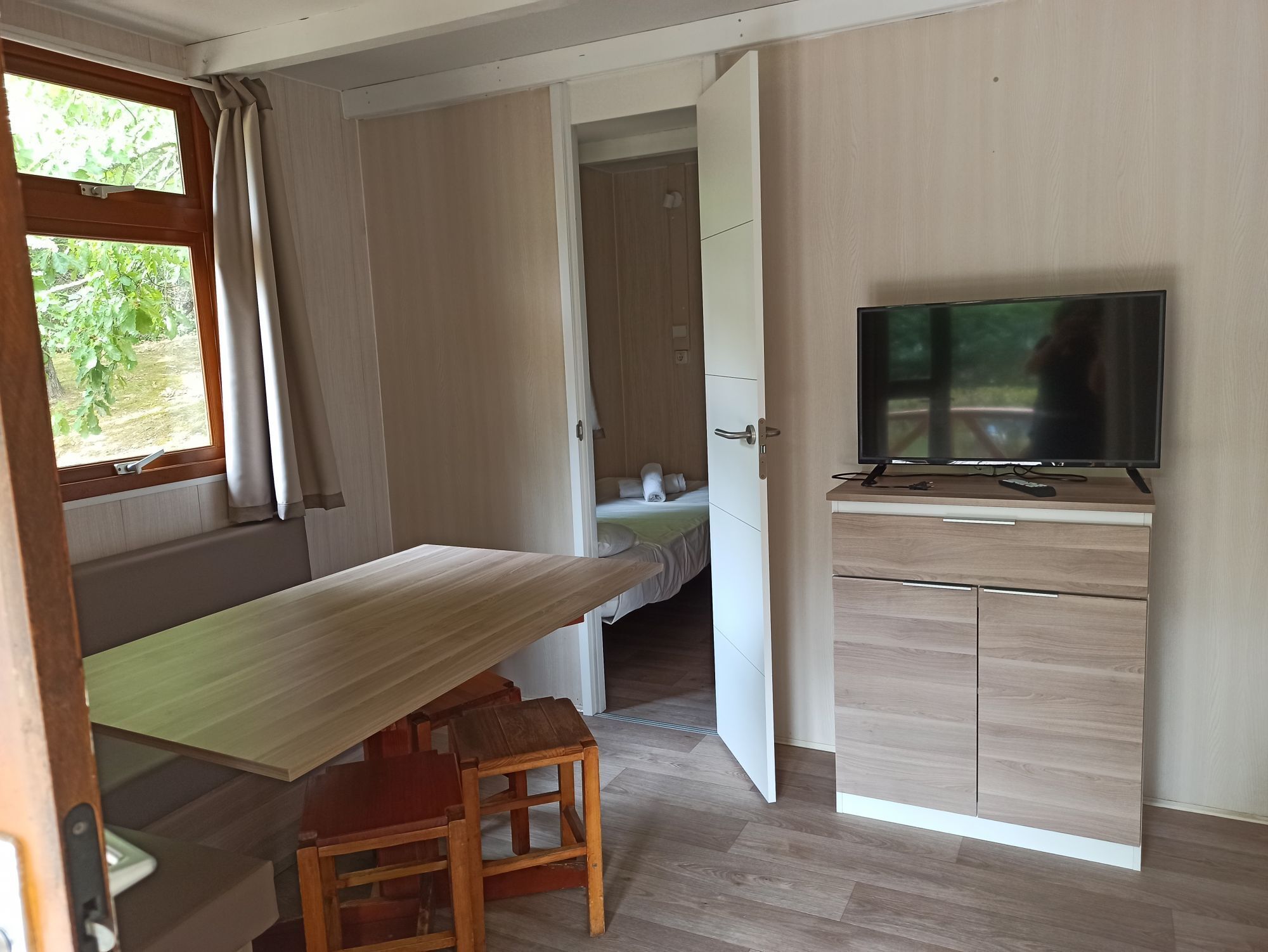 Una stanza compatta con una scrivania in legno, una televisione e un letto con vista sul verde.