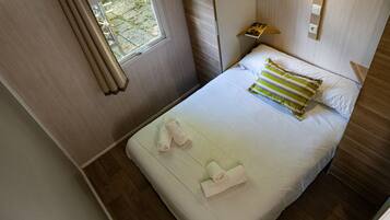 Una cama bien hecha con dos toallas, una ventana con cortinas y una mesita de noche con un libro.