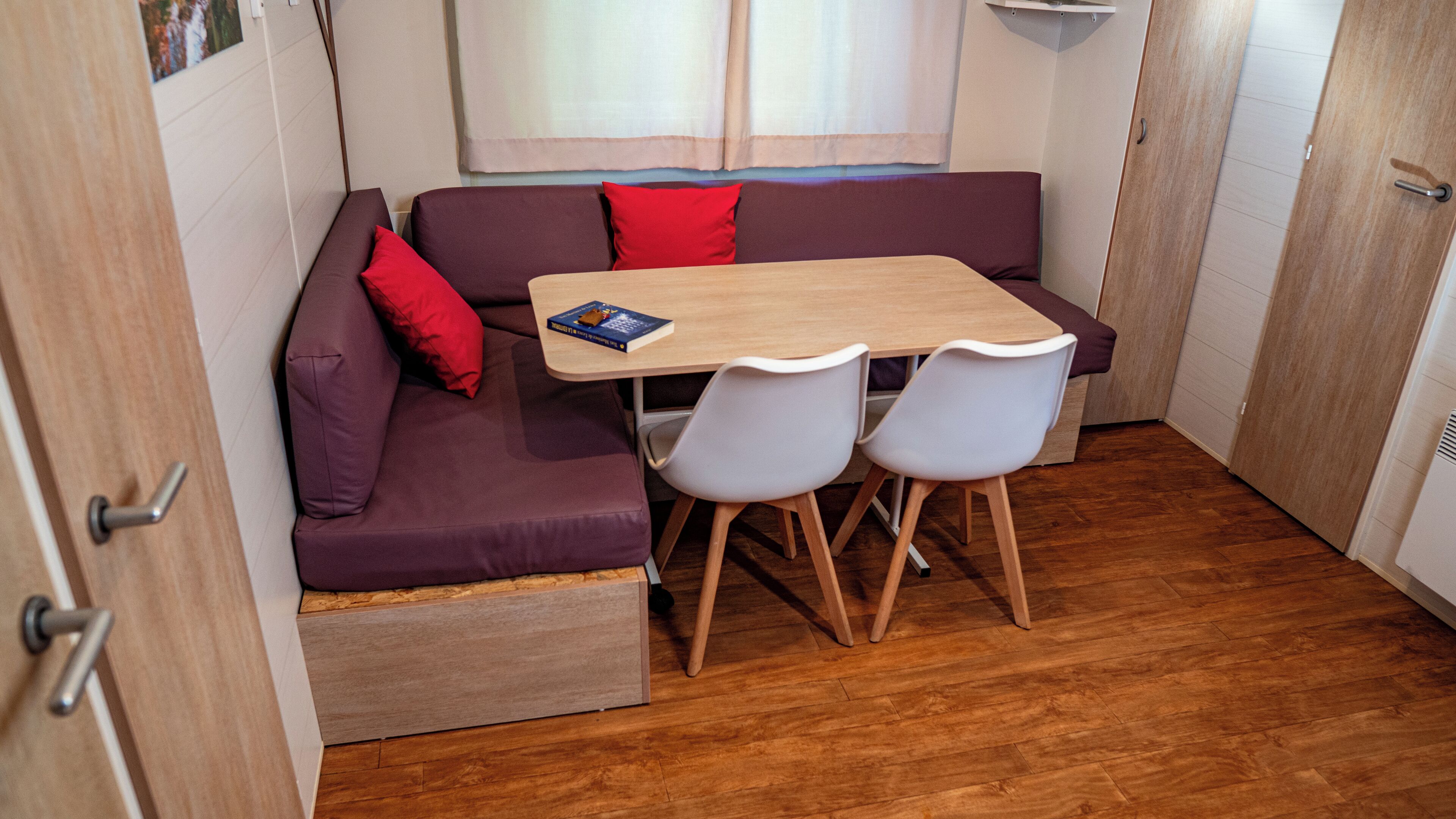 Een compact keukenhoekje met een houten tafel, twee stoelen en een ingebouwde bank met kussens.
