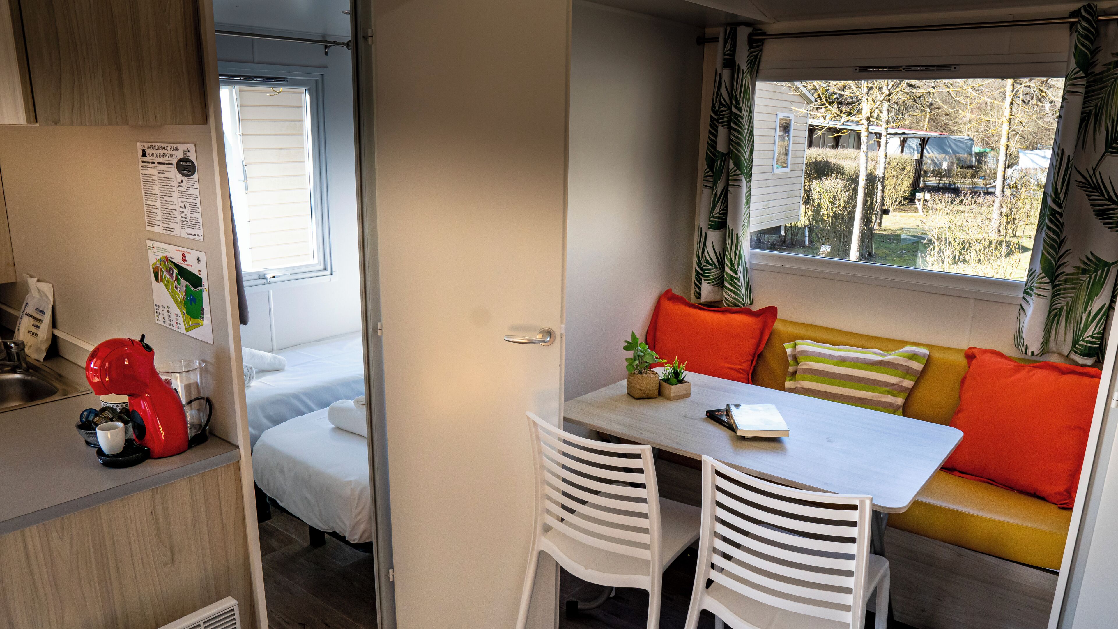 A compact RV interior with a kitchenette, a dining area, and a seating area with a view of the outdoors.