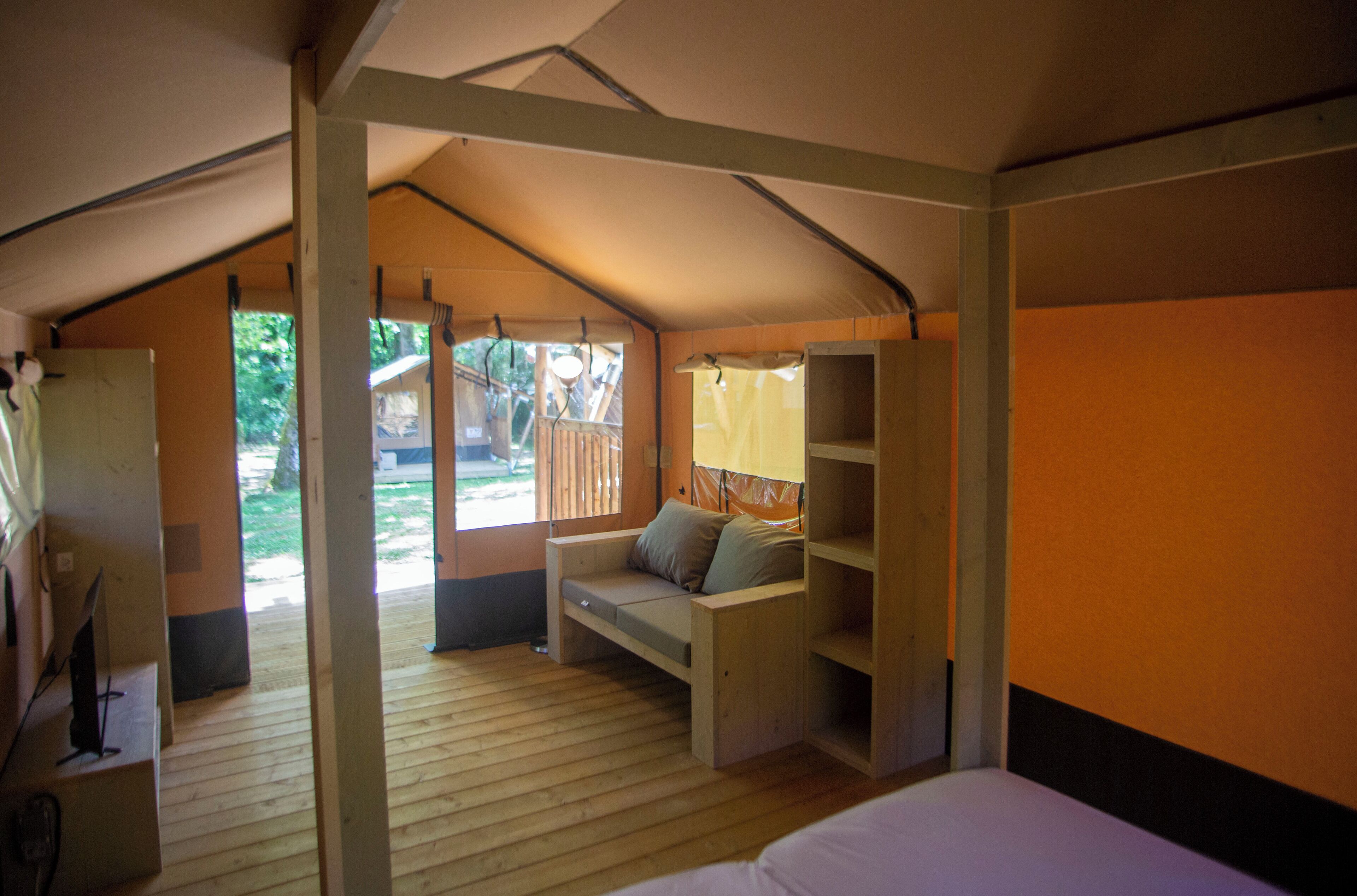 Alojamiento con tienda de campaña, suelo de madera, cama, zona de estar con cojines y estantería.