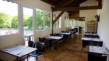 Un espace repas avec des tables dressées, de grandes fenêtres et une vue sur l’extérieur.