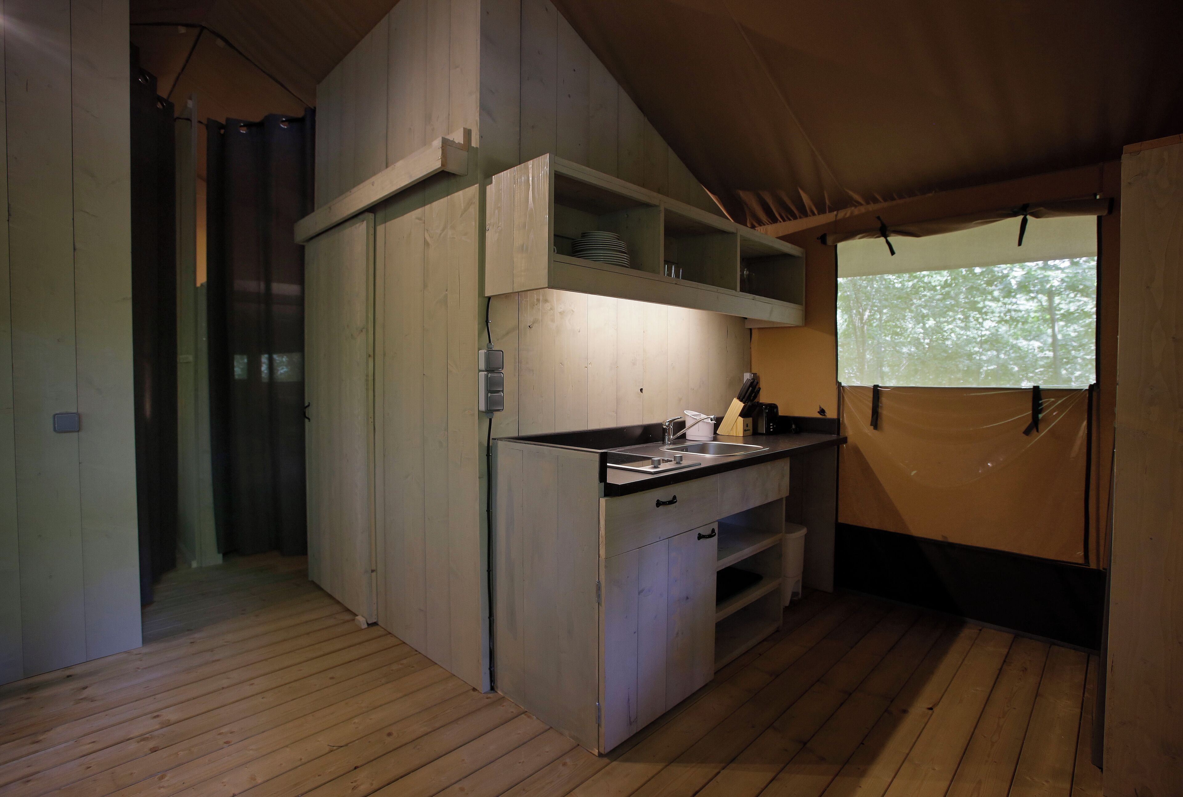 A compact kitchen with wooden cabinets, a sink, and a window with a view of trees.