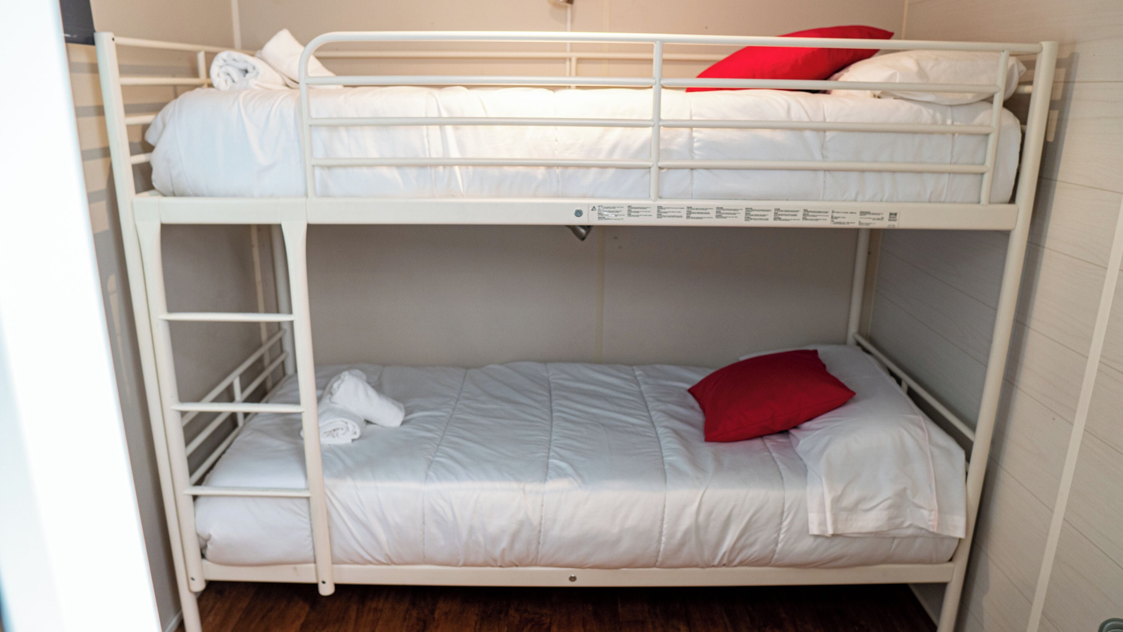 Un lit superposé avec une literie blanche et un oreiller rouge.