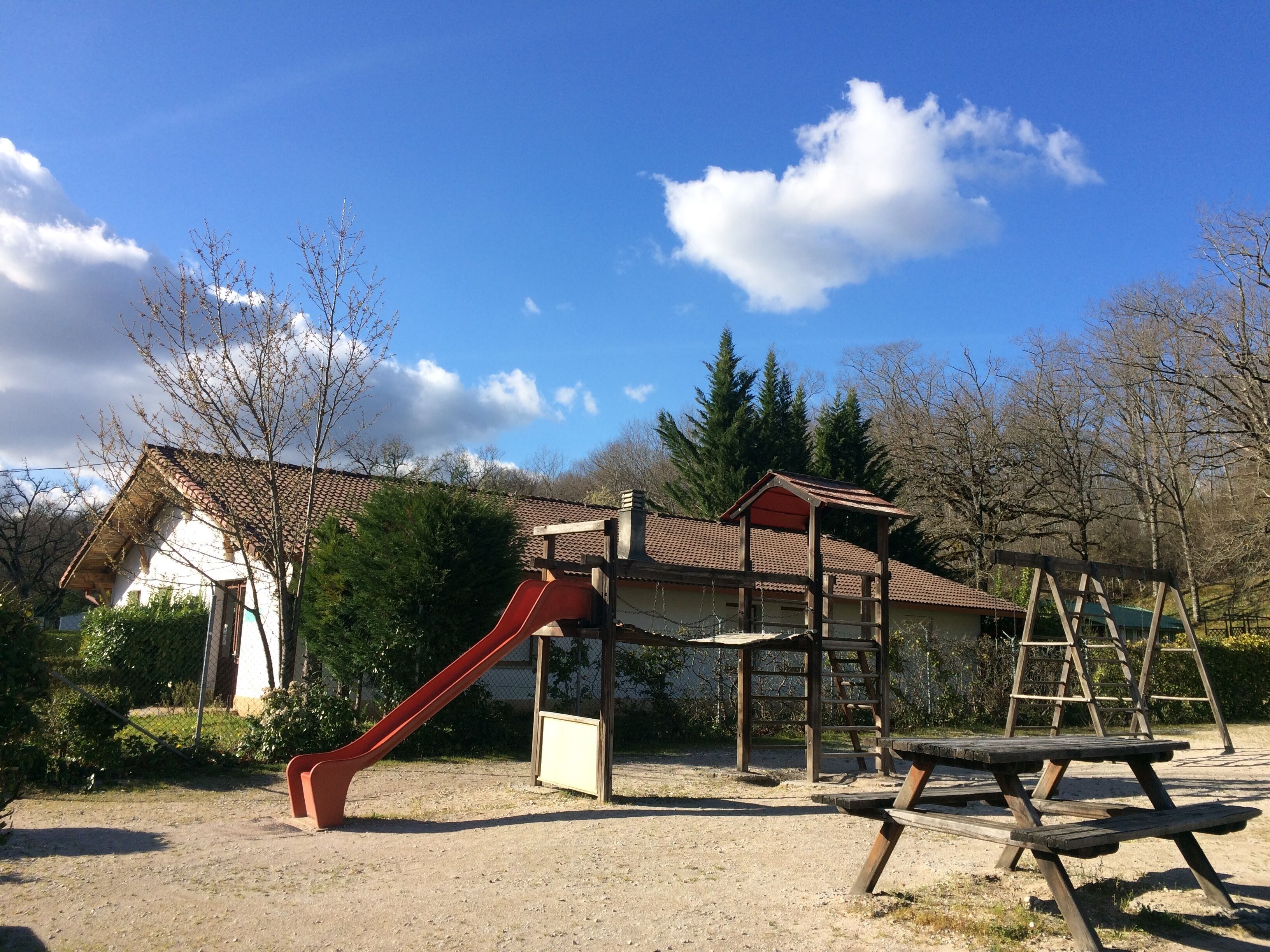 Un parque infantil con tobogán, columpios y mesas para picnic.