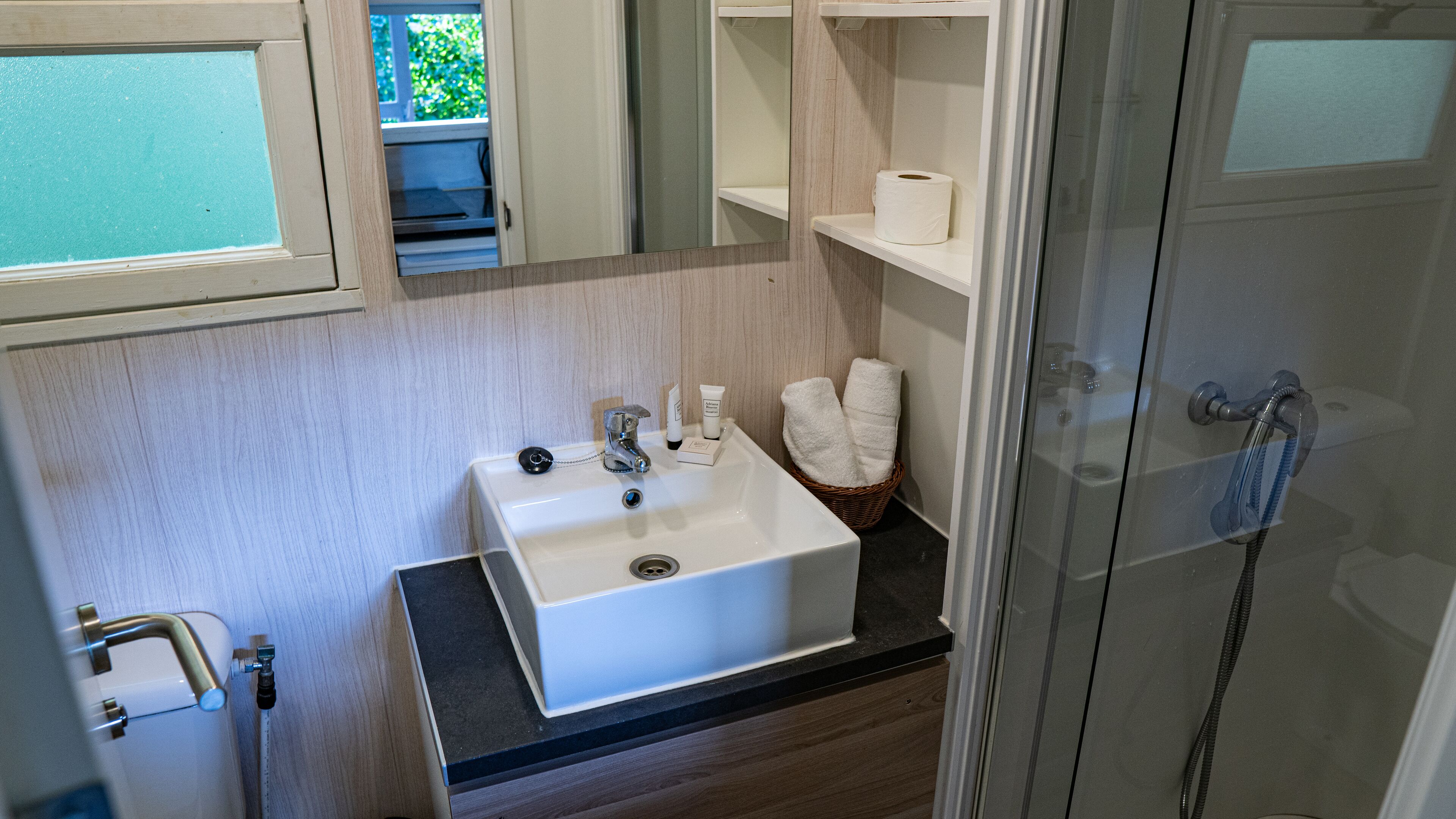 Un baño con lavamanos blanco, espejo, ducha y ventana.