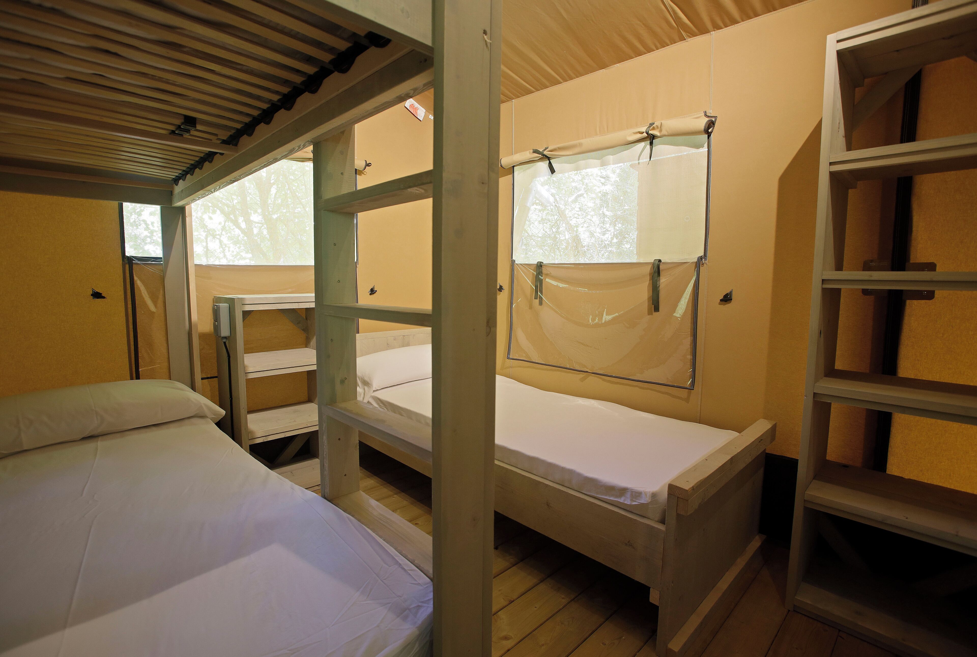 A dormitory room with bunk beds, a window with a curtain, and a shelf unit.