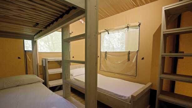 A dormitory room with bunk beds, a window with a curtain, and a shelf unit. - Camping Etxarri (Etxarri-Aranatz)