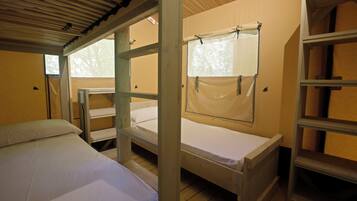 A dormitory room with bunk beds, a window with a curtain, and a shelf unit.