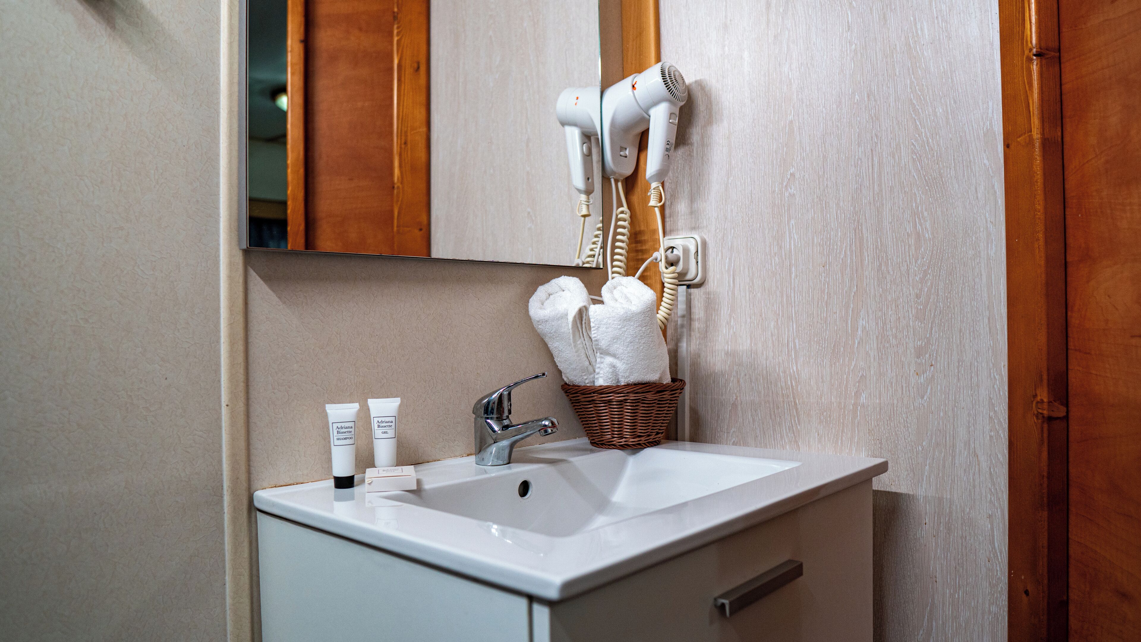 A bathroom with a white sink, a mirror, a hairdryer, and a basket with towels.