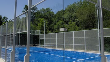 Instalación deportiva con cancha azul, cercado de metal y árboles al fondo.