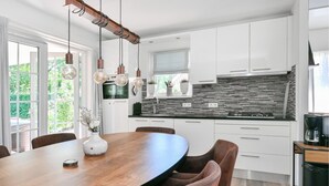 Una cocina moderna con armarios blancos, un salpicadero negro y una mesa de comedor de madera.