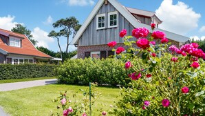 Una casa de dos pisos con techo de tejas rojas, fachada de ladrillo y un jardín bien cuidado con flores rosas.