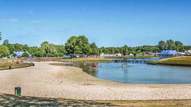 Una playa con un lago tranquilo, tiendas de campaña y una orilla arenosa.