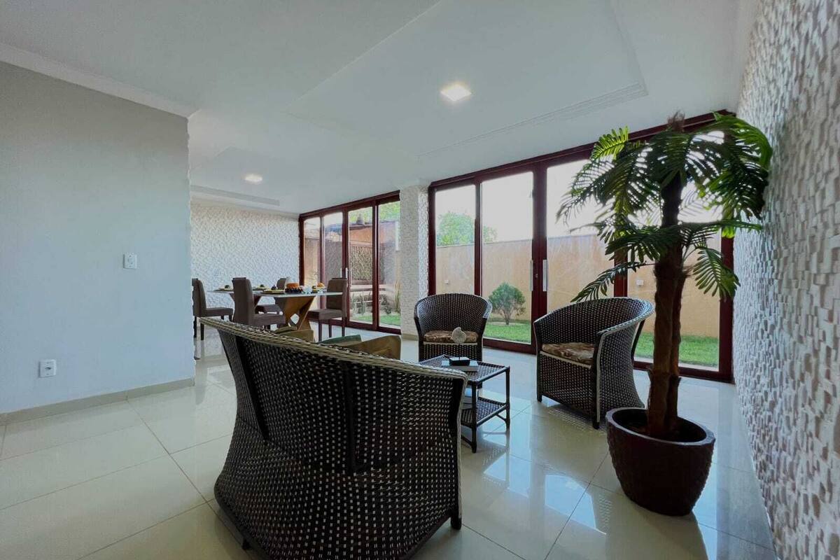 Un salón amplio con mesa de comedor, muebles de mimbre y una gran planta en maceta.