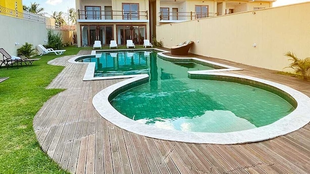 Zona de piscina amb dues piscines, una coberta de fusta i un edifici amb balcons.