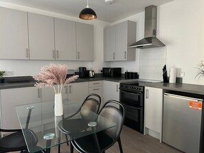 A modern kitchen with grey cabinets, a glass dining table, and black chairs. - Immaculate 2-bed Apartment in East London (London)