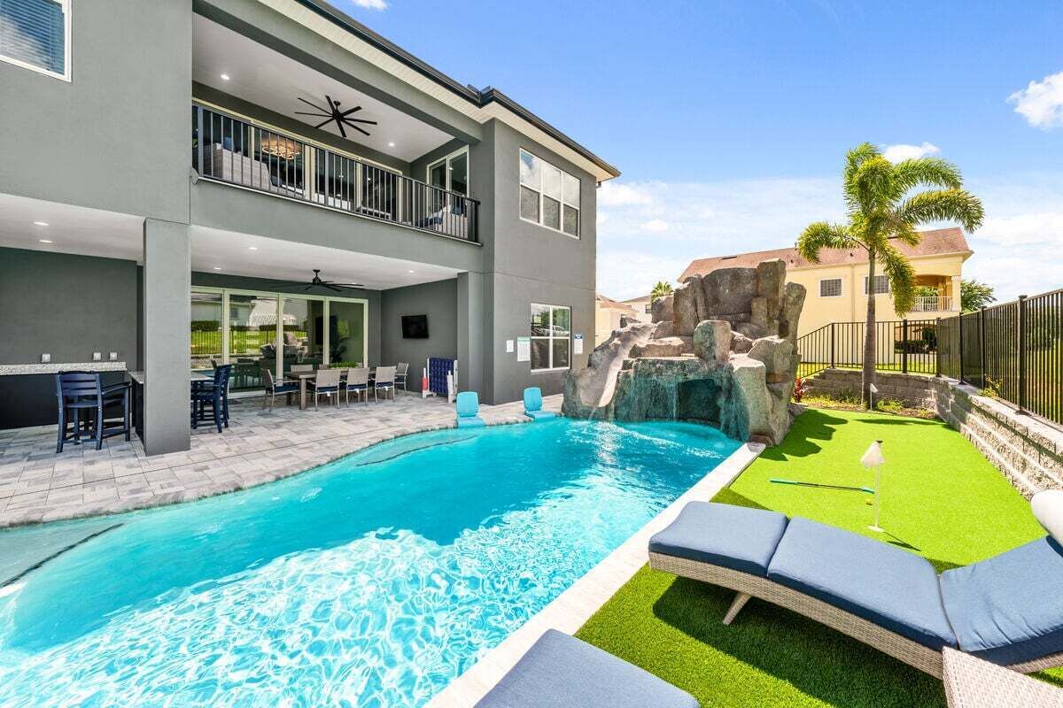 A modern two-story house with a swimming pool, outdoor seating, and a rock waterfall feature.