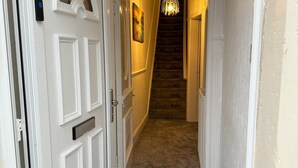 A hallway with a carpeted floor, a white door with the number 24, and a staircase leading to another floor. - Stunning 3-bedroom in Rishton (Blackburn)