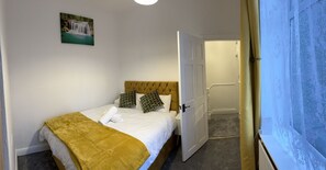 A neatly made bed with a yellow blanket, a headboard with a tufted design, and patterned pillows. - Stunning 3-bedroom in Rishton (Blackburn)