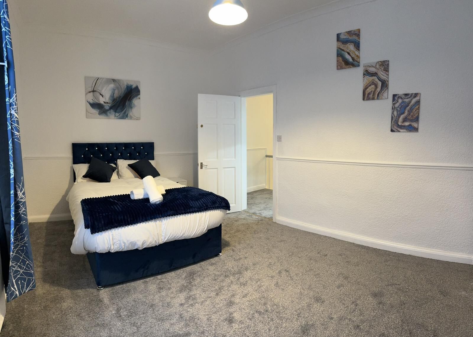 Une chambre à coucher avec un lit, une porte blanche et trois tableaux abstraits accrochés au mur.