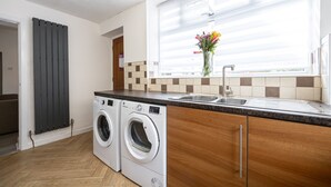 A modern kitchen with a built-in washer and dryer, a large window with blinds, and a wooden countertop. - Immaculate 3-bed House in Accrington (Accrington)