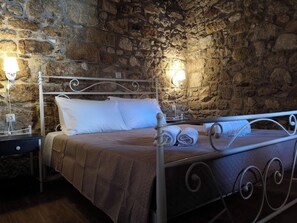 Een slaapkamer met stenen wanden, een metalen bed en witte beddengoed, met twee bedlampen.