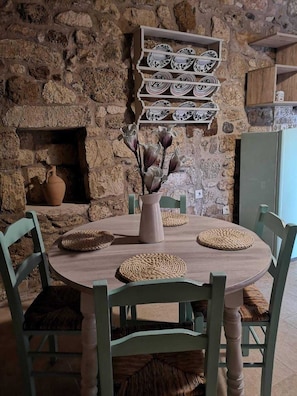 A stone wall, a round wooden table with woven placemats, and chairs with cushioned seats. - M & M Stone House in Massari (Rhodes)
