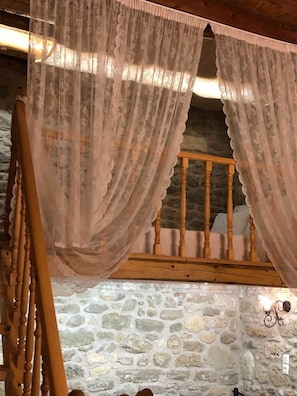 A rustic room with a stone wall, a wooden bench, and sheer curtains. - M & M Stone House in Massari (Rhodes)