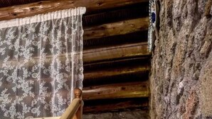 Un escalier en bois, orné d’un rideau en dentelle, mène à un mur de pierre sur lequel est fixée une applique murale.