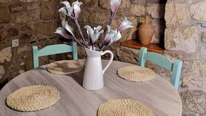 Une table ronde ornée d’un vase blanc rempli de fleurs, de quatre sets de table en fibres tressées et de deux chaises bleu clair.