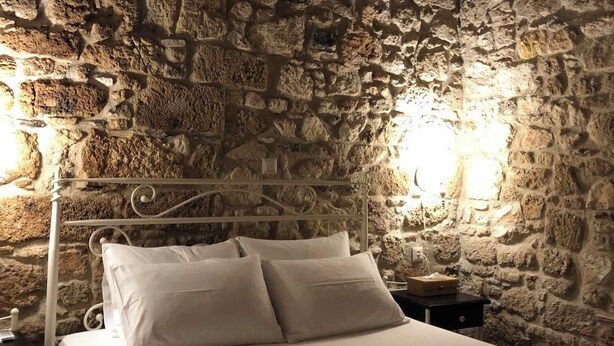 Une chambre aux murs de pierre, avec un lit, des oreillers blancs et une tête de lit en métal.