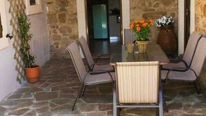Une terrasse dallée de pierres, avec une table et des chaises, un pot de fleurs et une cheminée.