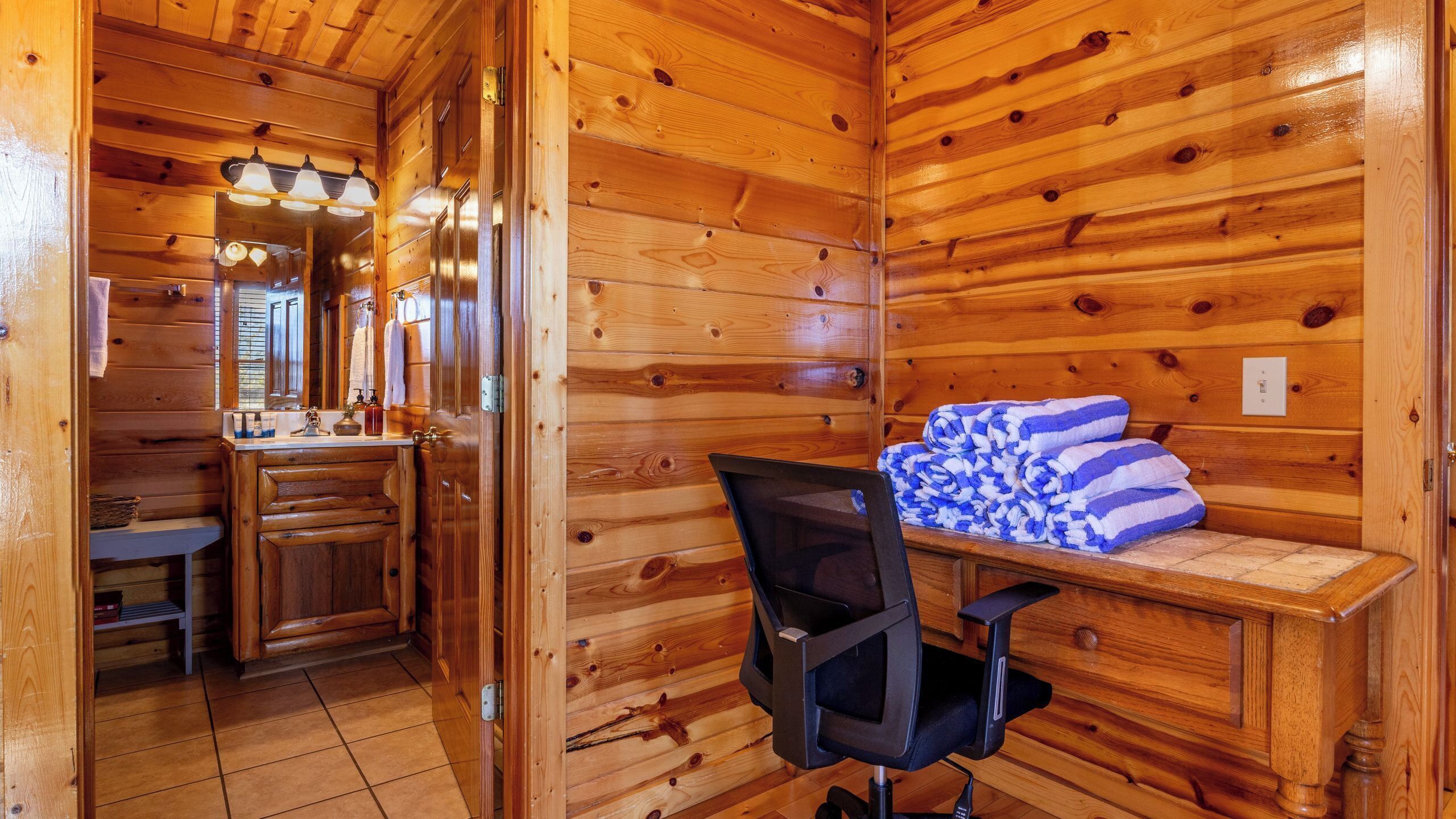 Ein Holzhütten-Interieur mit Bad, Schreibtisch mit Stuhl und einem Bett mit Handtüchern.