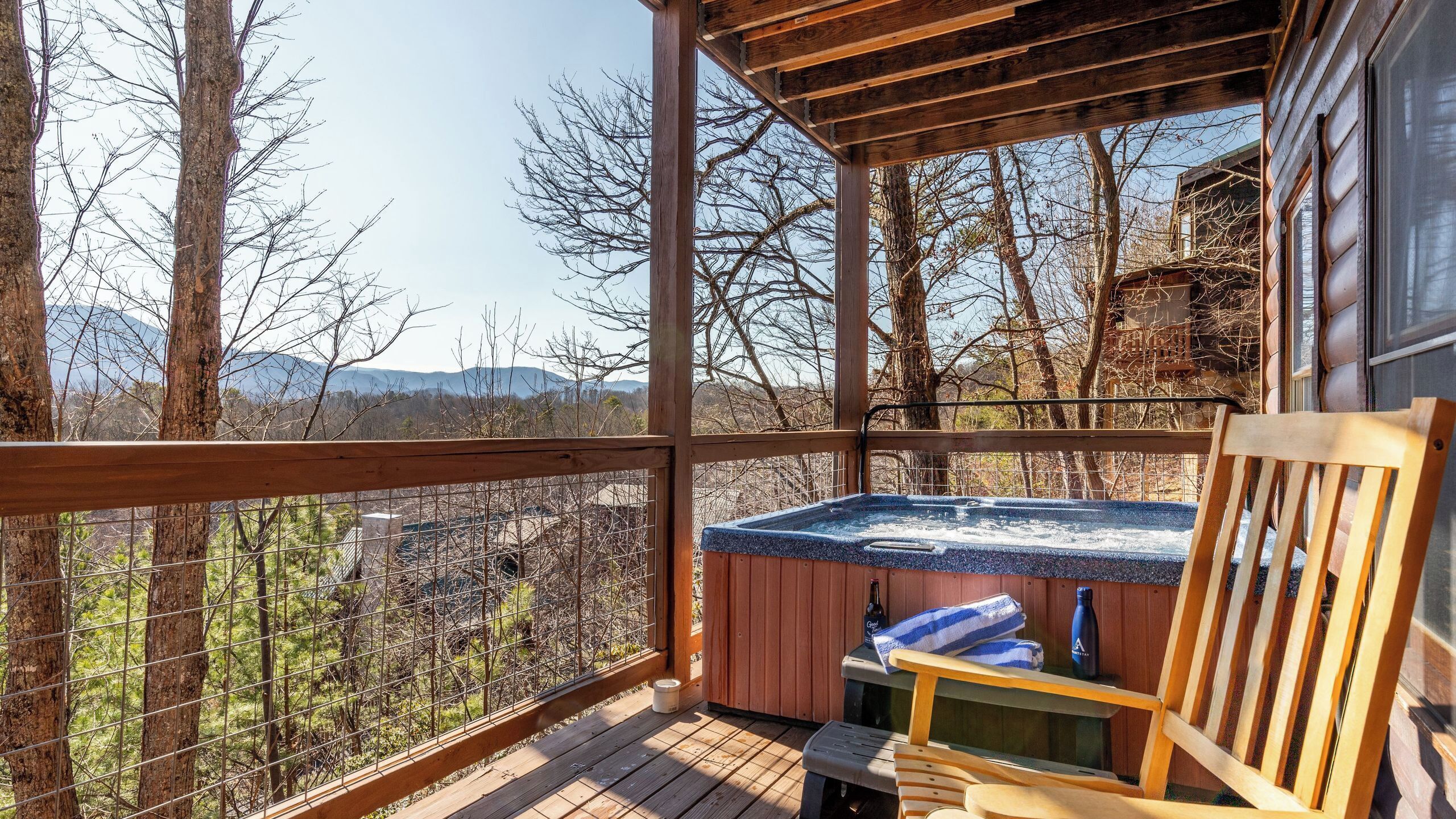 Een houten terras met een jacuzzi, een houten stoel en uitzicht op bomen en bergen.