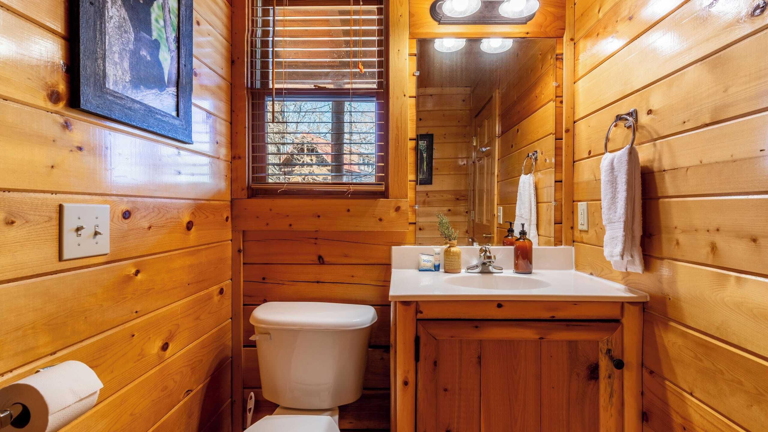 Un baño de madera pequeño y funcional con inodoro, lavamanos y ventana.