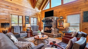 Un intérieur chaleureux de chalet en bois avec une cheminée, des meubles à motifs écossais et un mur décoratif en pierre.