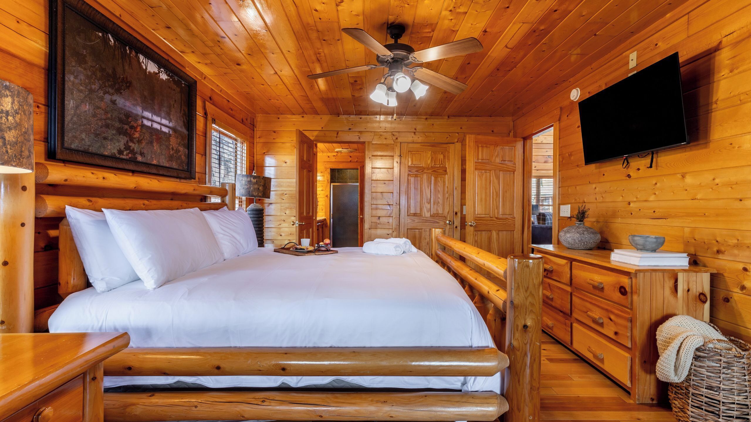 Una camera in una baita di legno, con un letto, una ventola a soffitto, una televisione e mobili in legno.