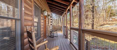 Une cabane en bois dotĂ©e dâune vĂ©randa, de fauteuils Ă bascule et offrant une vue sur la forĂȘt environnante.