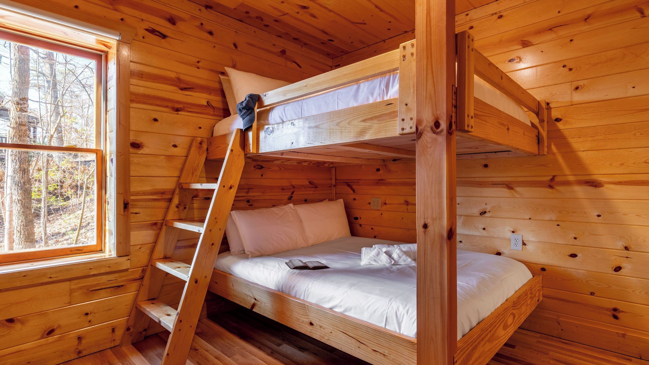 Een houten kamer met een stapelbed, een raam en een trap.