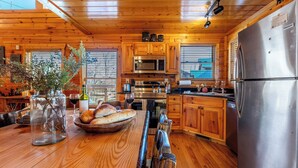 Une cuisine rustique dans une cabane en bois, avec une table en bois, un panier de pain, une bouteille de vin et un vase rempli de fleurs.